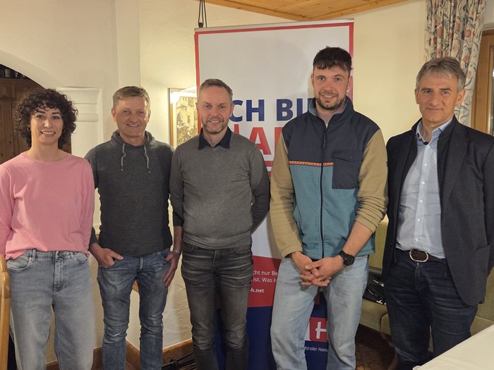 Handwerk bleibt tragende Säule in Gsies Fünf Personen stehen vor Banner in Zimmer bei Veranstaltung