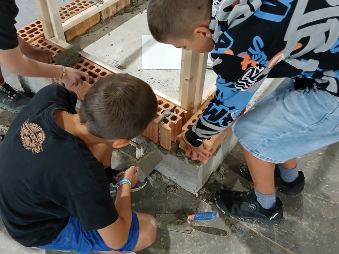 Mini-Baustelle, große Meisterwerke – KidsAcademy mauert in Bruneck Kinder bauen eine Mauer mit Ziegeln und Zement auf einem Bauplatz