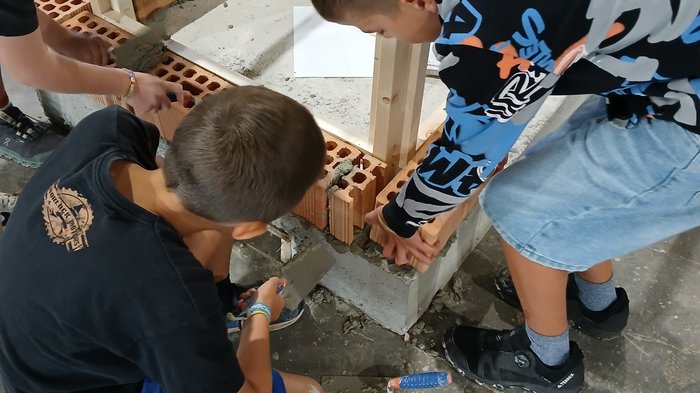 Mini-Baustelle, große Meisterwerke – KidsAcademy mauert in Bruneck Kinder bauen eine Mauer mit Ziegeln und Zement auf einem Bauplatz