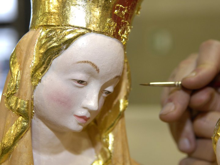 Policromatori e doratori Mano dipinge dettagli su statuetta religiosa tradizionale con decorazioni dorate