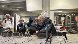 News Erwachsener zeigt Jugendlichen in Werkstatt Arbeit mit Metallformen