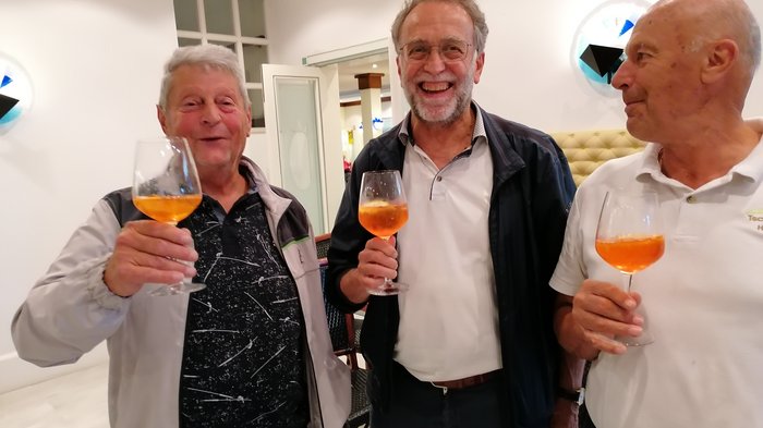 Badespaß an der Adria Drei ältere Männer stoßen mit Orangencocktails in einem Innenraum an.