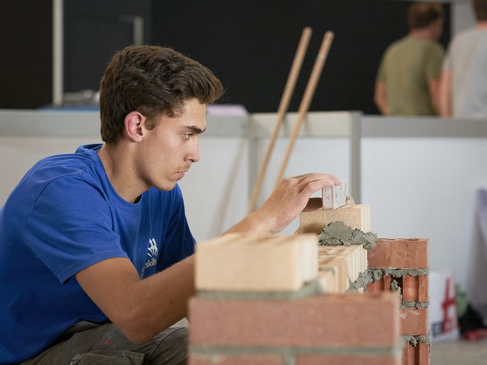 Handwerk live: Junge Talente zeigen, was sie draufhaben Junger Bauarbeiter mauert konzentriert eine Wand aus Ziegelsteinen im Innenbereich