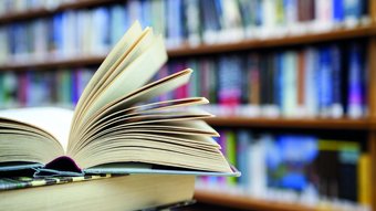Veranstaltungen Offenes Buch mit umgeschlagenen Seiten vor Bücherregal in Bibliothek