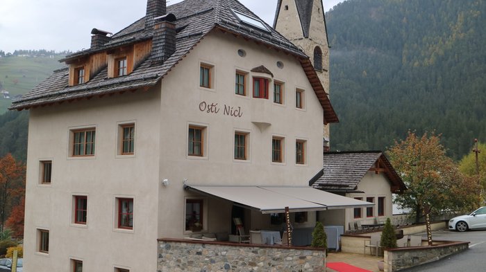 Neuauflage: Plattform Land startet 2. Sanierungsberatung für Private und Gemeinden Traditionelles Gasthaus Ostì Nicl vor bewaldetem Berg in ruhiger Landschaft