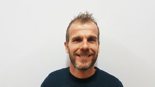 News Lächelnder Mann mit kurzen Haaren und Bart vor weißem Hintergrund