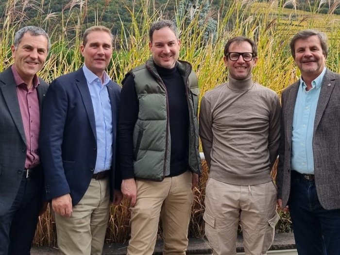 Gemeinsam für sichere Energiezukunft: 3-Ländertreffen der Kaminkehrer/innen in Südtirol! Fünf lächelnde Männer stehen vor Gräsern im Freien