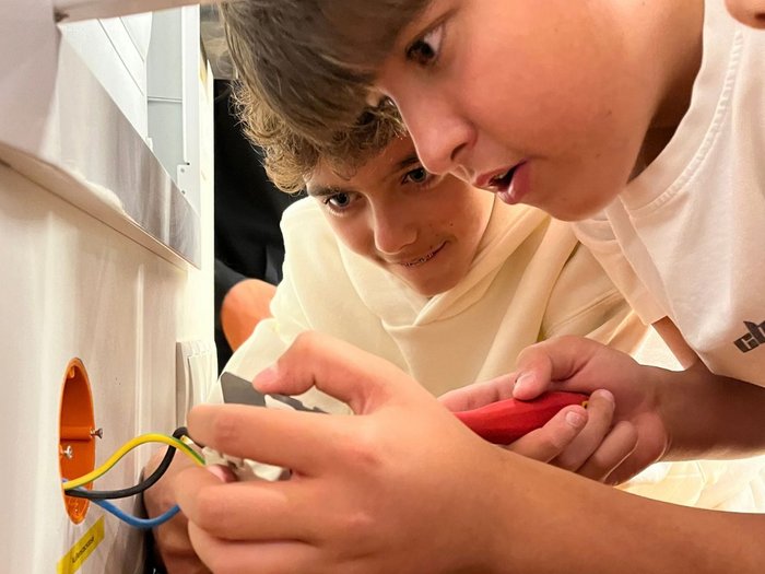 SkillsDay a Vipiteno: Mettersi all’opera Due ragazzi esaminano cavi colorati in una presa a muro aperta