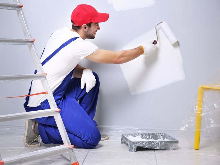 Pittori e verniciatori Uomo con berretto rosso pittura muro bianco con rullo