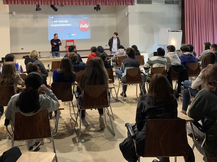 A Bolzano i giovani scoprono i mestieri nei settori dell’artigianato e dell’ospitalità Giovani seduti in aula che ascoltano due relatori davanti