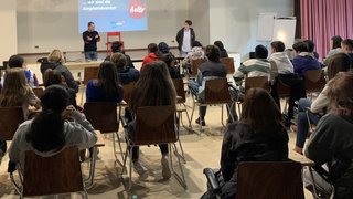 News Jugendliche sitzen in einem Seminarraum und hören zwei Vortragenden zu