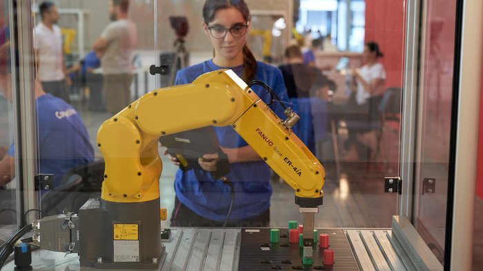 Handwerk live: Junge Talente zeigen, was sie draufhaben Frau bedient gelben Industrieroboter bei Schulungsübung in Werkstatt