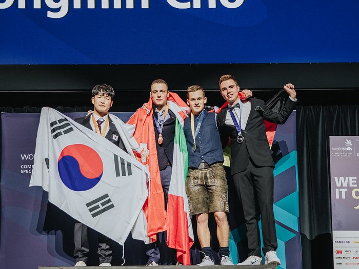 WorldSkills in Bozen: Bronzemedaille und Medallion for Excellence für zwei Südtiroler Gewinner auf Podium mit Flaggen von Südkorea, Wales, Italien und Deutschland