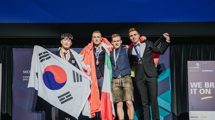 WorldSkills in Bozen: Bronzemedaille und Medallion for Excellence für zwei Südtiroler Gewinner auf Podium mit Flaggen von Südkorea, Wales, Italien und Deutschland