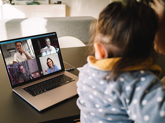Arbeit und Familie unter einem Hut Frau mit Kind nimmt an Videoanruf mit vier Personen auf Laptop teil