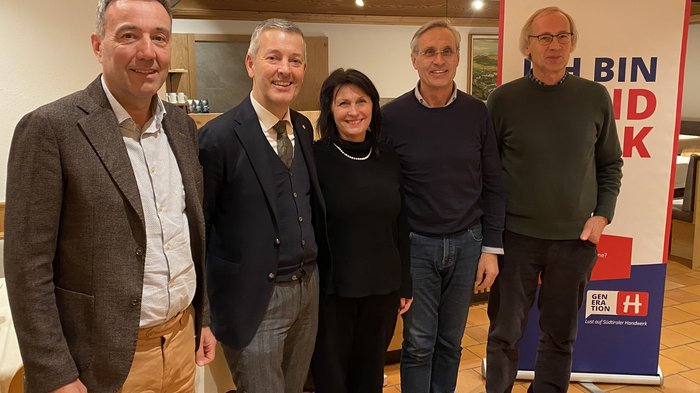 Serata informativa a Malles Venosta: focus su pianificazione territoriale e promozione dei giovani talenti Cinque persone insieme davanti a uno striscione pubblicitario in ambiente interno