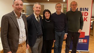 News Fünf Personen stehen zusammen vor einem Werbebanner in einem Innenraum