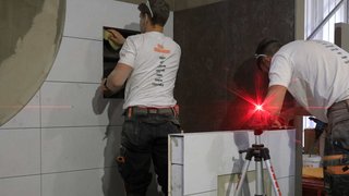News Zwei Handwerker verlegen Fliesen und verwenden Lasertechnik für Präzision
