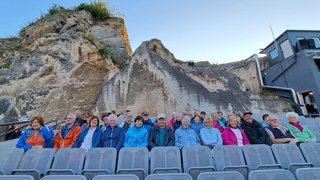 News Senioren sitzen auf Sitzreihen vor einer Felsenwand im Freilufttheater