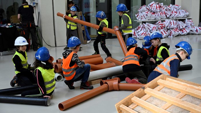 Einen Tag auf der Baustelle erleben Kinder mit Schutzhelmen und Warnwesten bauen mit großen Rohren drinnen