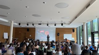 News Schulveranstaltung mit Referentin vor Schülern in modernem Saal