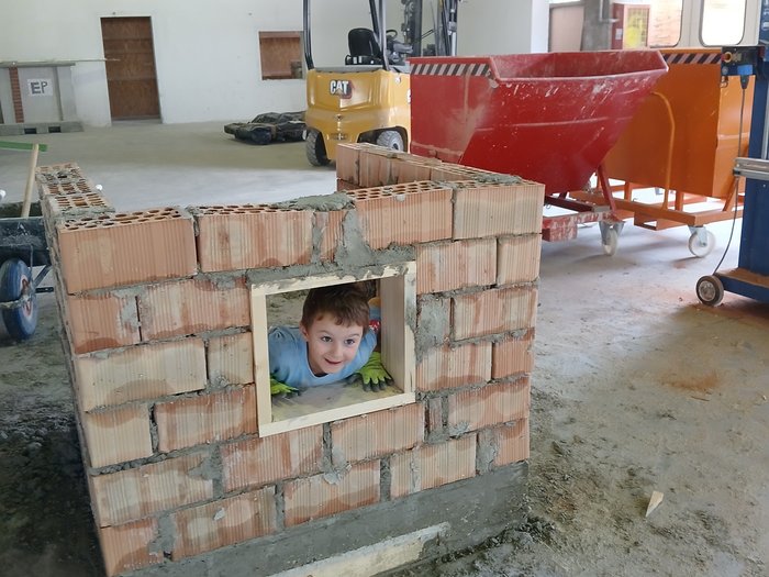 Kids Academy 2024: a Brunico l’artigianato colora l’estate dei più piccoli Bambino guarda attraverso finestra in muratura di mattoni in cantiere