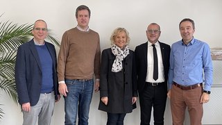 News Fünf Personen stehen vor einer weißen Wand und lächeln in die Kamera