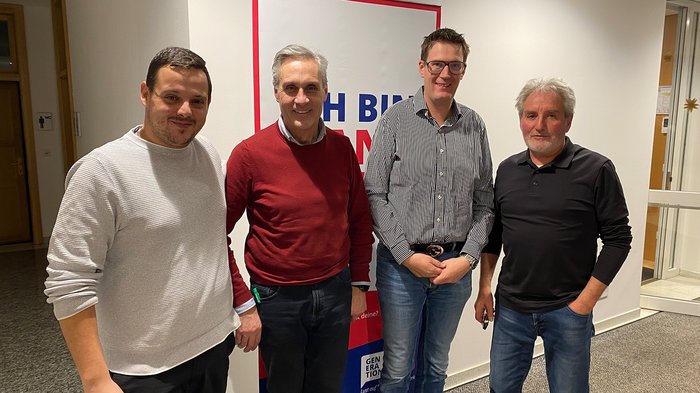 Südtirols Betriebe als stille Leistungsträger der Winterspiele Vier Männer stehen vor einem Plakat in einem Flur