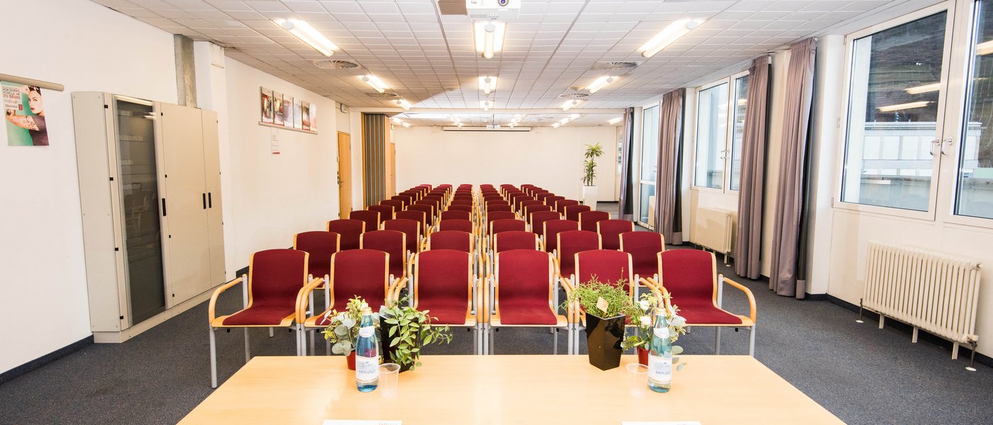 Affitto aule seminari Sala conferenze vuota con sedie rosse, tavolo con bottiglie d'acqua e piante