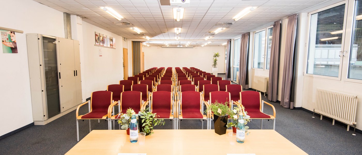 Vermietung Seminarräume Leerer Konferenzraum mit roten Stühlen, Tisch mit Wasserflaschen und Pflanzen