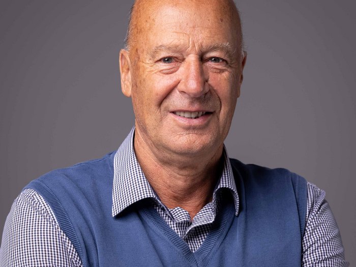 Neue Gesetzesdekrete zum Thema Senioren und Nichtselbstständigkeit Porträt eines lächelnden älteren Mannes mit blauem Pullover und kariertem Hemd vor grauem Hintergrund