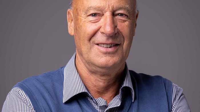 Neue Gesetzesdekrete zum Thema Senioren und Nichtselbstständigkeit Porträt eines lächelnden älteren Mannes mit blauem Pullover und kariertem Hemd vor grauem Hintergrund