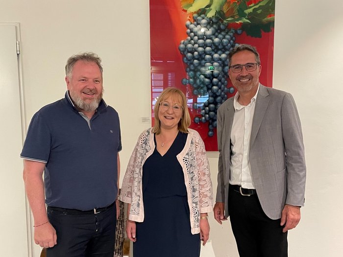 Gert Lanz, Petra Holzer und Arno Kompatscher © lvh.apa Drei lächelnde Personen vor einem Bild von Trauben an einer Wand