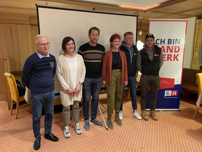 Junges Handwerk in Deutschnofen Sechs Personen stehen vor einer Leinwand und einem Banner in einem Veranstaltungsraum