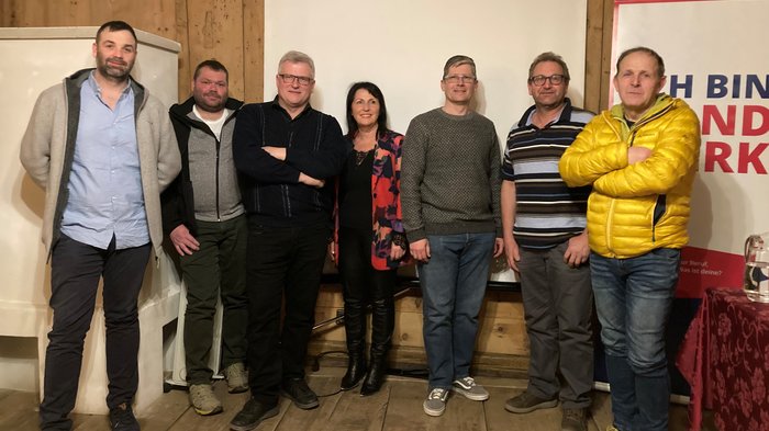 Neue lvh-Führung in Laas Sieben Personen stehen nebeneinander vor einer weißen Leinwand und einer Holzwand