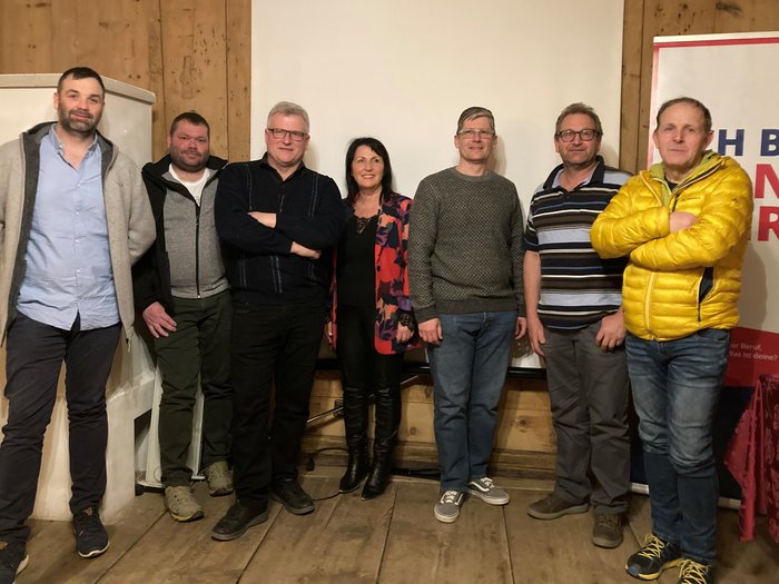 Neue lvh-Führung in Laas Sieben Personen stehen nebeneinander vor einer weißen Leinwand und einer Holzwand