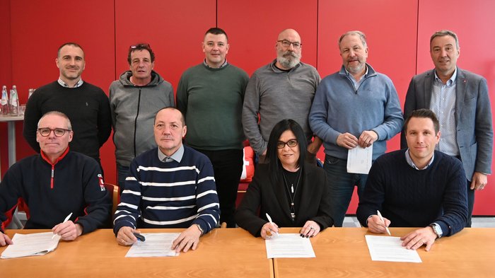 Variables Lohnelement auch für 2025 bestätigt Zehn Personen bei Vertragsunterzeichnung vor roter Wand