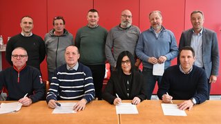 News Dieci persone firmano contratti davanti a parete rossa