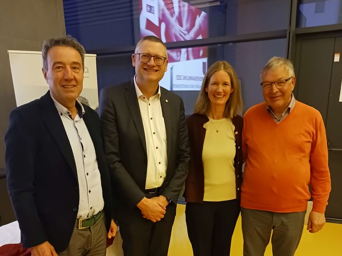 30 Jahre Berufsgemeinschaft Kälte- und Klimatechnik: Fachwissen, Nachwuchsförderung und Zukunftsausblick Vier Personen in formeller Kleidung stehen vor einem Fenster und lächeln