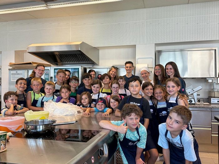 Mit Faden, Fantasie und Fingerfertigkeit – Die KidsAcademy in Brixen macht Handwerk erlebbar Kinder in Kochschürzen in einer modernen Großküche posieren für Gruppenfoto