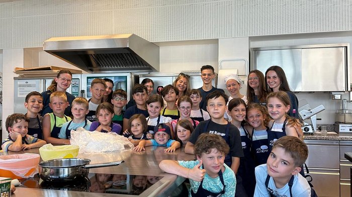 Creatività a misura di bambino: a Bressanone l’artigianato prende vita con la Kids Academy Bambini con grembiuli da cucina in una cucina professionale posano per foto di gruppo