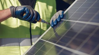News Handwerker montiert Solarmodul mit Schraubendreher und Handschuhen