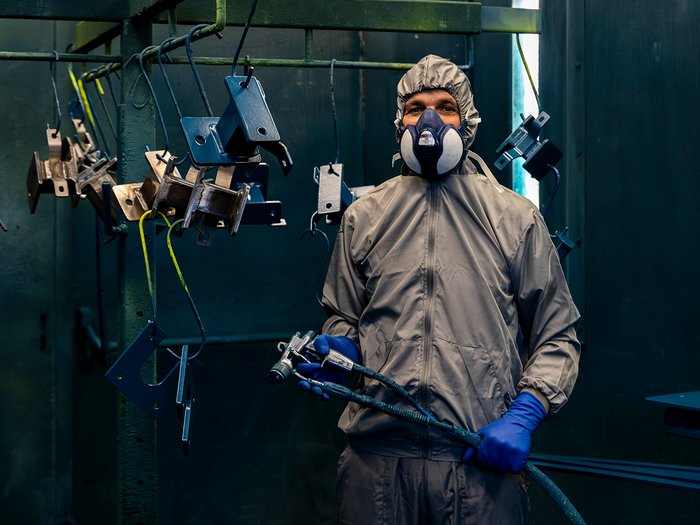La sicurezza è un lavoro fatto a mano Lavoratore con tuta protettiva e maschera mentre vernicia parti in metallo in fabbrica
