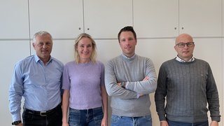 News Vier Personen stehen nebeneinander vor einem weißen Schrank