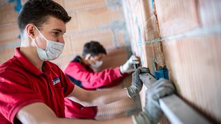 News Handwerker mit Maske messen Wand mit Wasserwaage bei Bauarbeiten