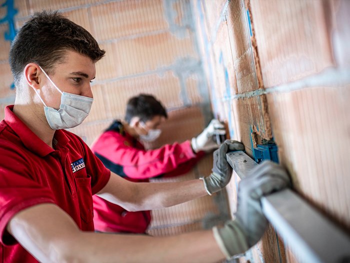 Öffentliche Aufträge: Wichtige Zusammenarbeit mit Alperia Handwerker mit Maske messen Wand mit Wasserwaage bei Bauarbeiten