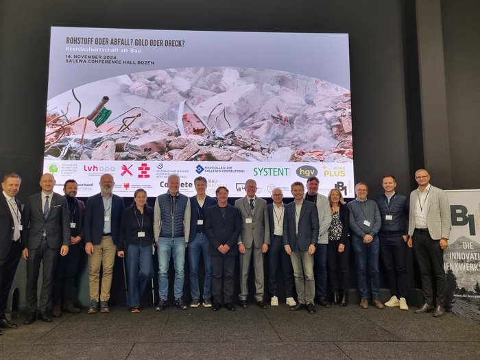 Fachtagung: "Kreislaufwirtschaft am Bau: Rohstoff oder Abfall? Gold oder Dreck?" Gruppenfoto vor einer Präsentation zum Thema Kreislaufwirtschaft am Bau in Bozen