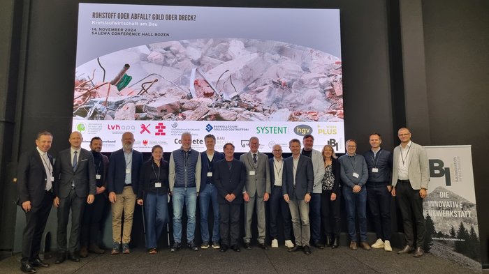 Fachtagung: "Kreislaufwirtschaft am Bau: Rohstoff oder Abfall? Gold oder Dreck?" Gruppenfoto vor einer Präsentation zum Thema Kreislaufwirtschaft am Bau in Bozen