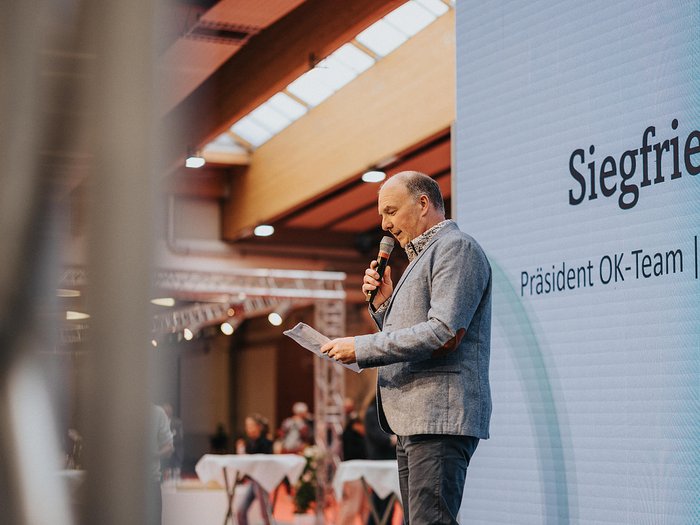 Grande successo all’inaugurazione della Fiera dell'Economia della Val d'Isarco a Bressanone - una vetrina per mostrare la vitalità dell’economia locale Uomo con microfono legge da foglio durante evento davanti a schermo di presentazione