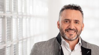 News Lächelnder Mann vor einer Wand mit Glasbausteinen